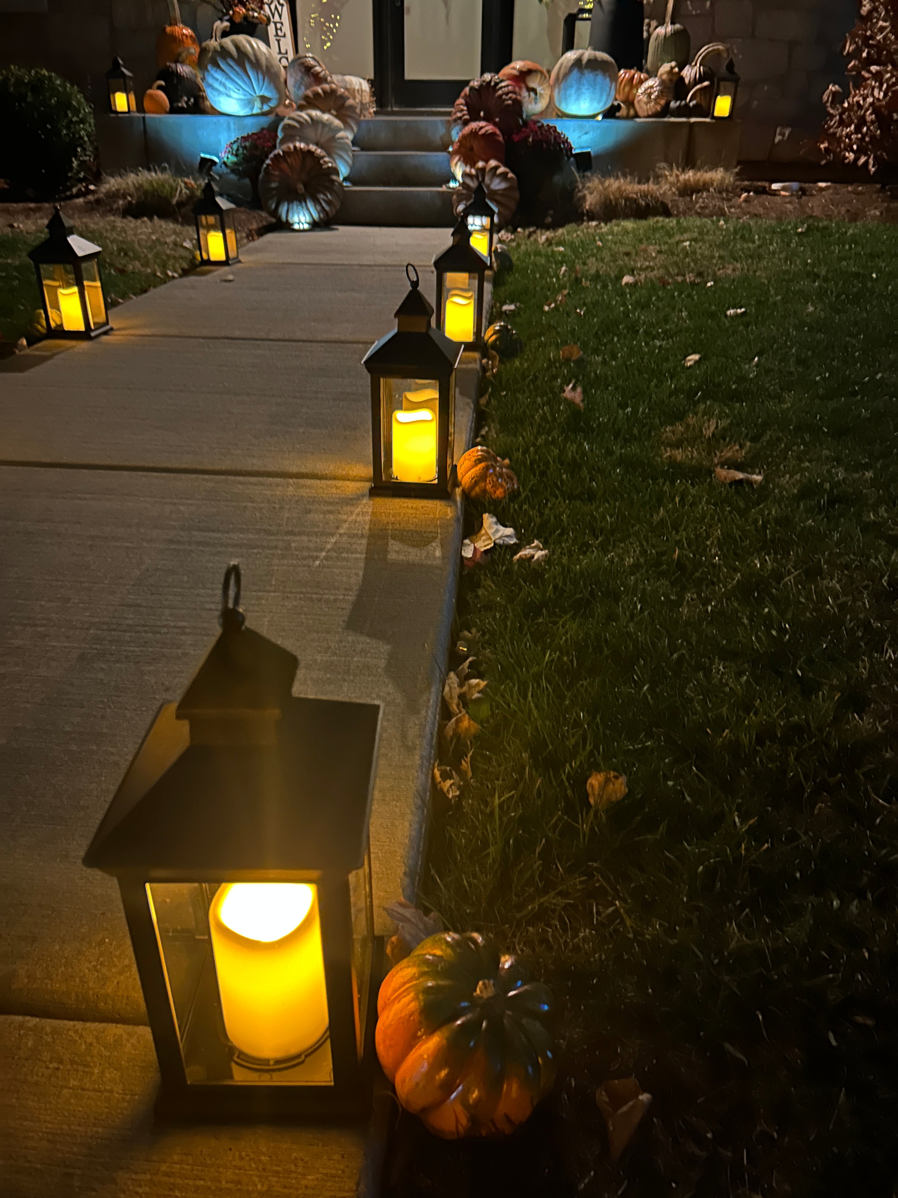 Decorative outdoor setting with lit lanterns and pumpkins on a wooden fence at night.