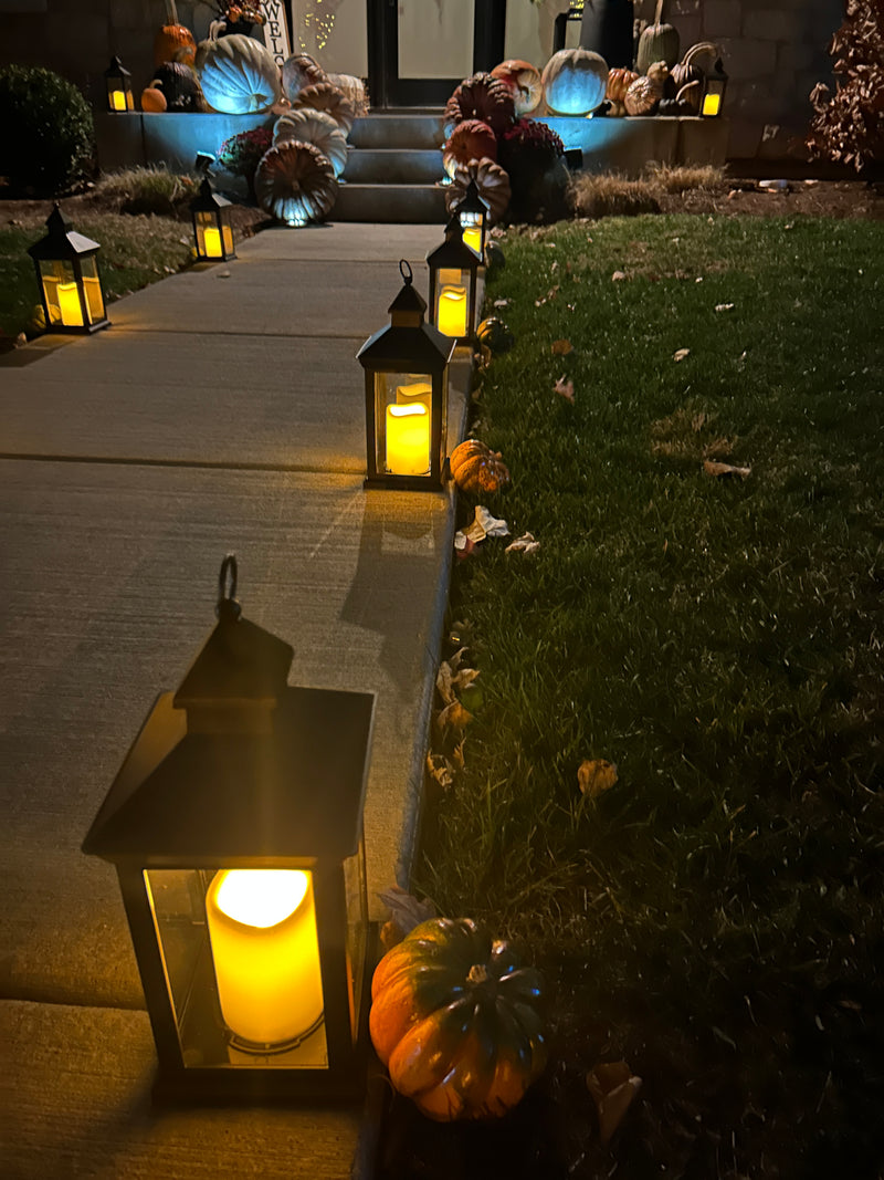 Decorative outdoor setting with lit lanterns and pumpkins on a wooden fence at night.