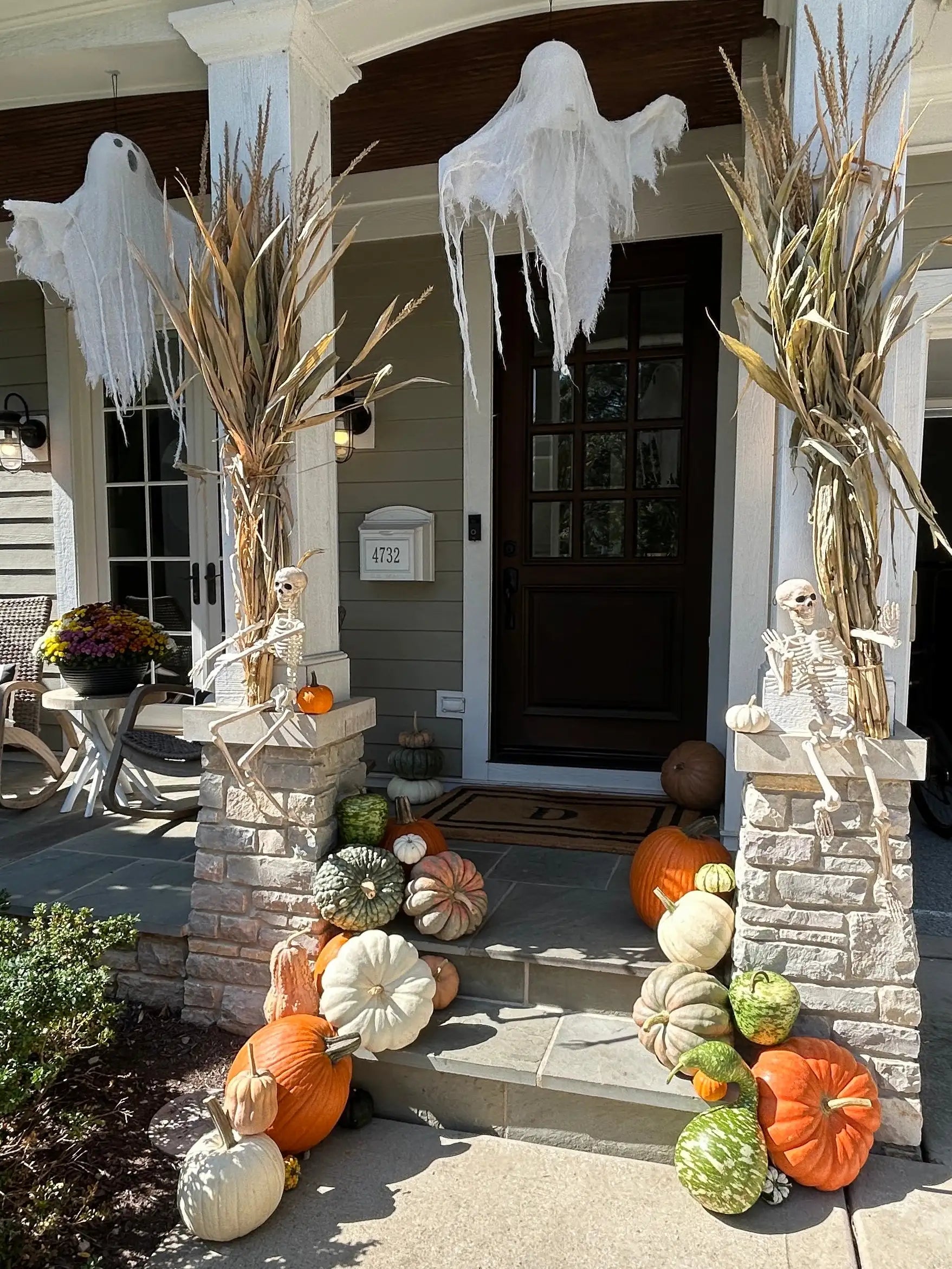 Halloween decorations on a front porch with pumpkins, ghosts, and skeletons.